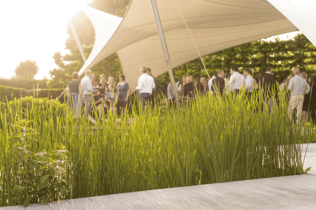 Gasten verzamelen in de tuin voor een babyborrel, met groen gras op de voorgrond en een feestelijke sfeer onder een groot wit zeil