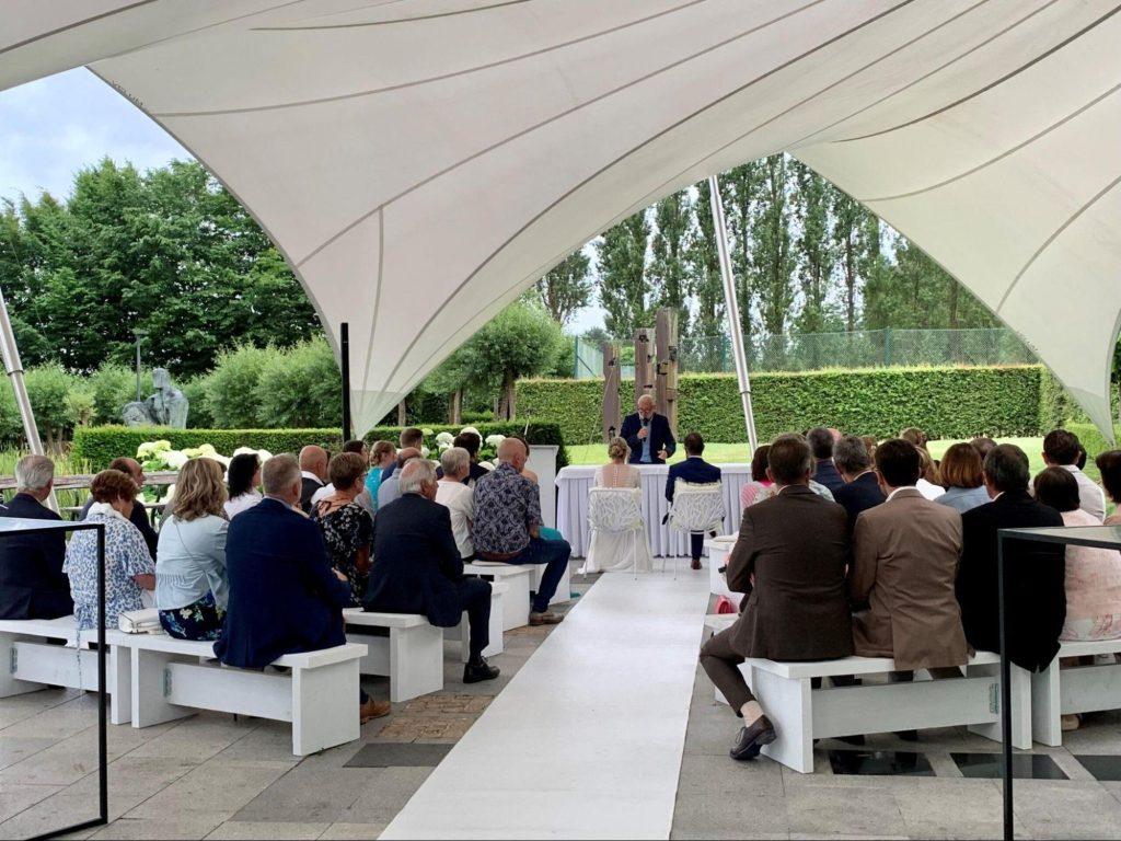 Intieme trouwceremonie met gasten zittend onder een moderne overkapping.