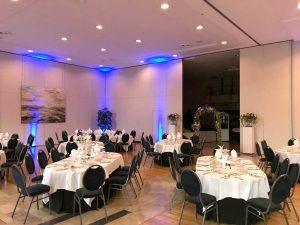 Salle de fête dressée pour un événement d’entreprise avec éclairage d’ambiance et disposition de table élégante.